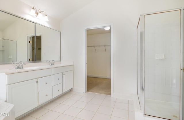 bathroom featuring double vanity, a walk in closet, a shower stall, a sink, and baseboards