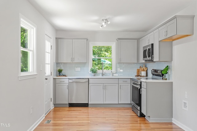 kitchen featuring stainless steel appliances, backsplash, light wood finished floors, and light countertops