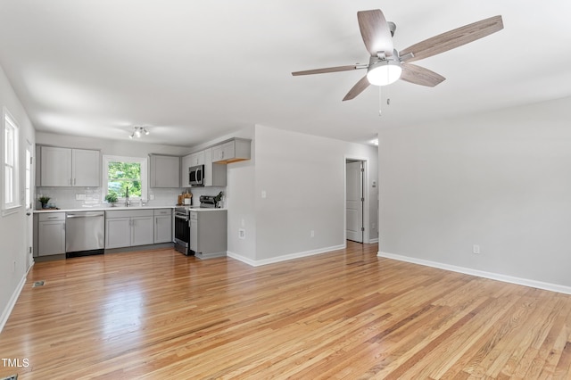 unfurnished living room with a sink, light wood-type flooring, baseboards, and ceiling fan