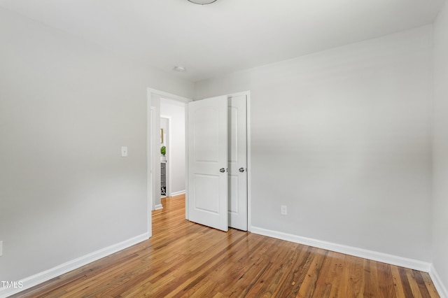 unfurnished bedroom featuring baseboards, wood finished floors, and a closet