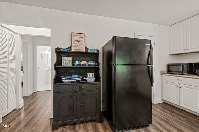 kitchen featuring dark wood-style flooring, baseboards, white cabinets, freestanding refrigerator, and stainless steel microwave