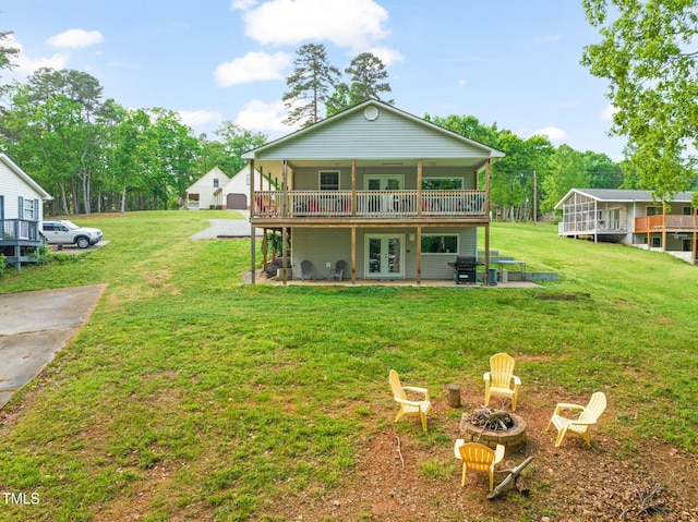 rear view of property featuring a lawn, an outdoor fire pit, a wooden deck, and french doors