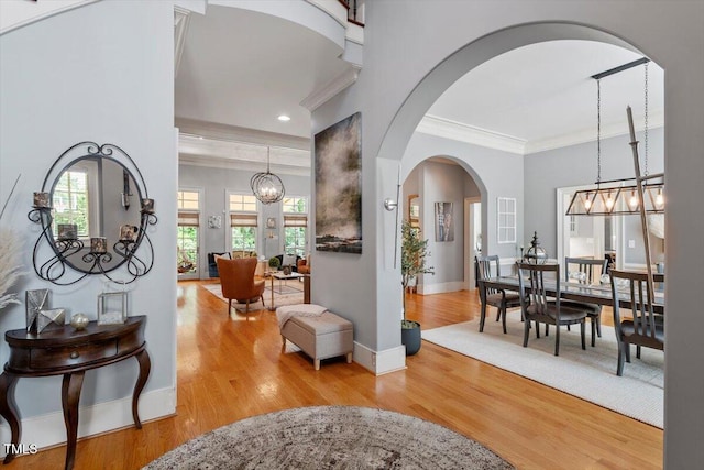 entrance foyer featuring crown molding, wood finished floors, arched walkways, baseboards, and a chandelier