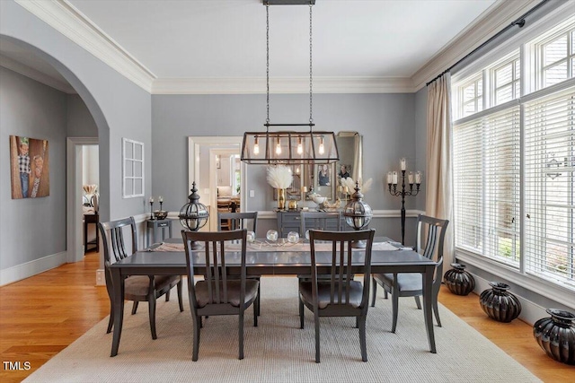 dining room featuring arched walkways, wood finished floors, crown molding, and baseboards