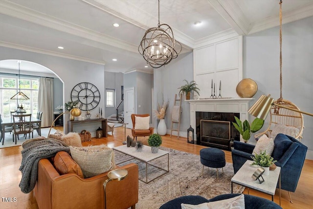 living area featuring a chandelier, crown molding, arched walkways, light wood finished floors, and beamed ceiling