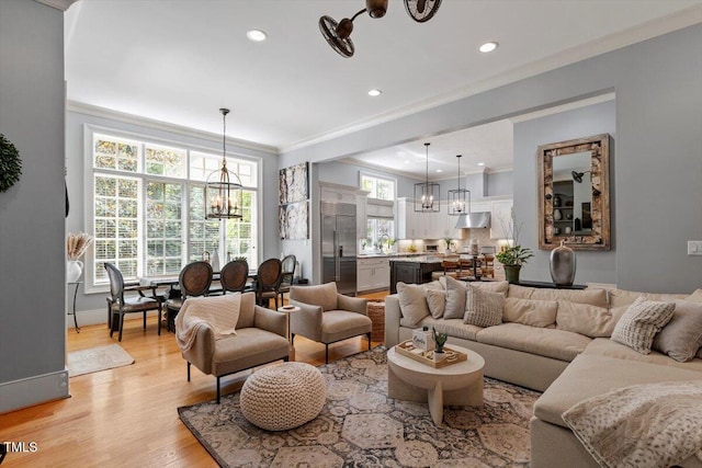 living area featuring a chandelier, light wood-style floors, ornamental molding, and recessed lighting