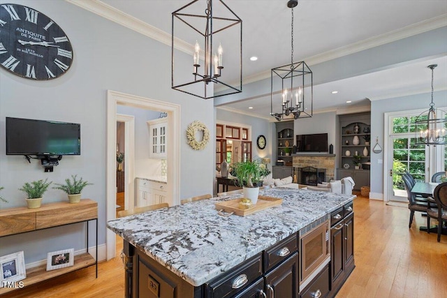 kitchen featuring a chandelier, stainless steel microwave, light wood finished floors, light stone countertops, and pendant lighting