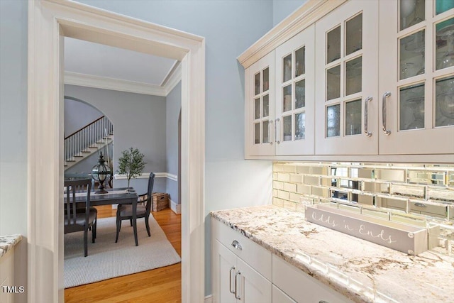 bar area with light wood-style flooring, crown molding, stairway, arched walkways, and decorative backsplash