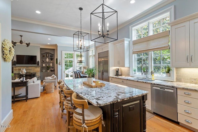 kitchen featuring stainless steel appliances, a sink, ornamental molding, a chandelier, and open floor plan