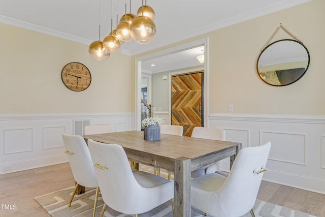 dining area with a decorative wall, light wood-style floors, a wainscoted wall, visible vents, and ornamental molding