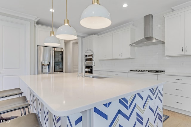 kitchen with wall chimney range hood, a kitchen breakfast bar, a kitchen island with sink, appliances with stainless steel finishes, and a sink