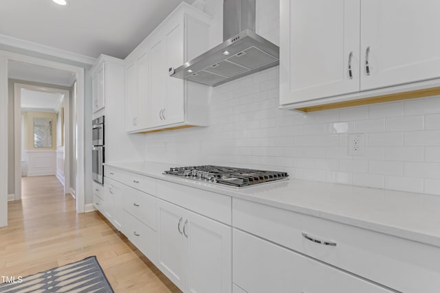 kitchen featuring appliances with stainless steel finishes, light countertops, wall chimney exhaust hood, white cabinetry, and decorative backsplash
