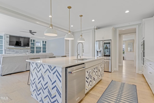 kitchen with white cabinets, appliances with stainless steel finishes, a sink, a kitchen island with sink, and light countertops