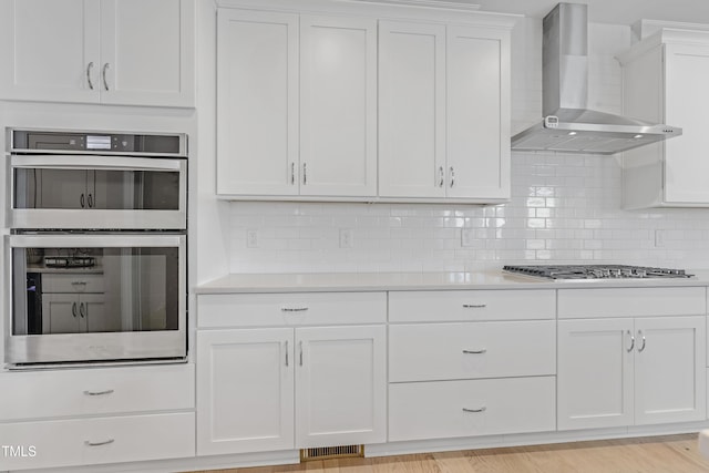 kitchen featuring light countertops, stainless steel appliances, white cabinetry, and wall chimney exhaust hood