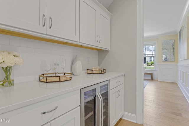bar featuring crown molding, decorative backsplash, beverage cooler, a bar, and light wood-style flooring