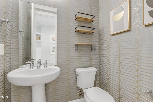 bathroom with a sink, toilet, and wallpapered walls