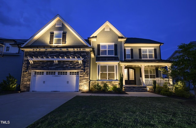 craftsman-style home with stone siding, a standing seam roof, concrete driveway, a lawn, and covered porch