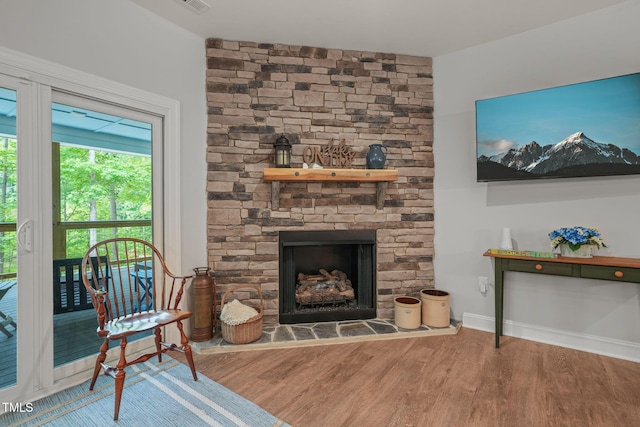 living room featuring baseboards, a stone fireplace, wood finished floors, and visible vents