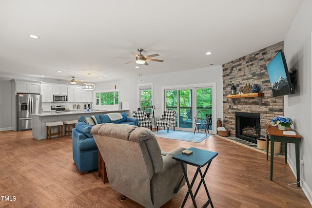 living area featuring a fireplace, a ceiling fan, recessed lighting, and wood finished floors
