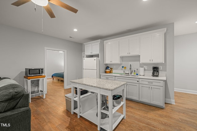 kitchen featuring white cabinets, a sink, freestanding refrigerator, recessed lighting, and stainless steel microwave