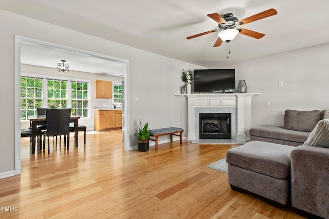 living area with light wood-style floors, baseboards, a fireplace, and a ceiling fan