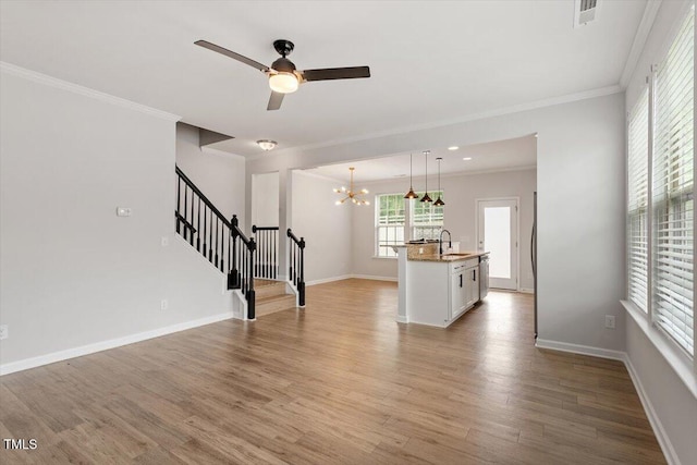 unfurnished living room with a sink, crown molding, stairway, a chandelier, and light wood finished floors