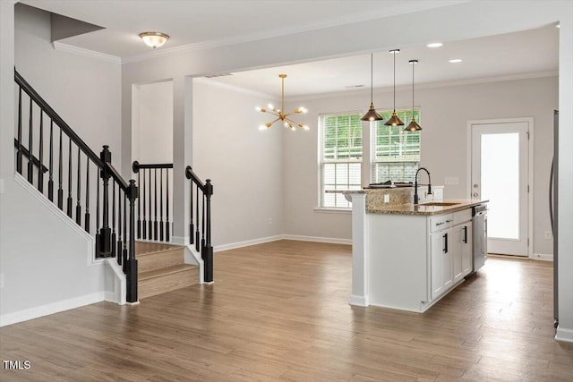 kitchen featuring a sink, stainless steel dishwasher, light stone counters, light wood-type flooring, and hanging light fixtures