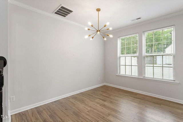 empty room with a chandelier, healthy amount of natural light, wood finished floors, ornamental molding, and baseboards