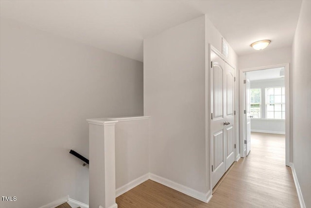 hallway with an upstairs landing, wood finished floors, and baseboards