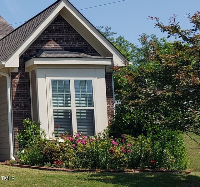 view of side of home featuring a yard, brick siding, and roof with shingles