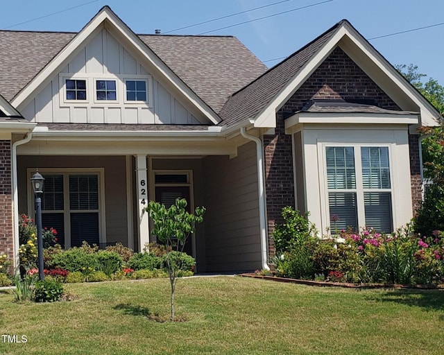 view of front facade with roof with shingles, board and batten siding, a front lawn, and brick siding