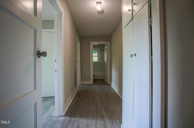 hallway featuring light wood-style floors, baseboards, and a textured ceiling