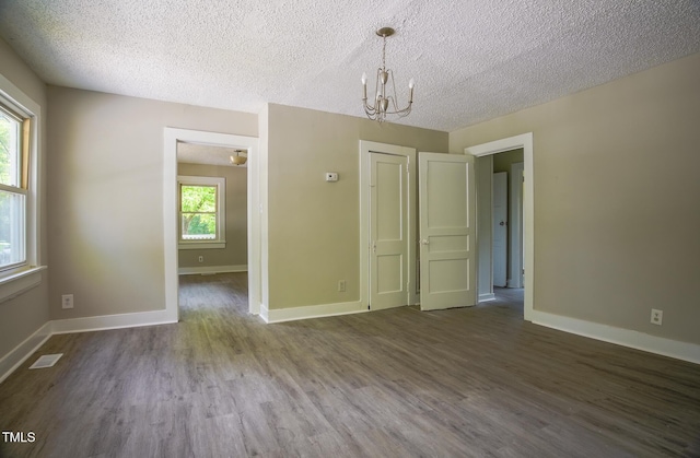 unfurnished dining area featuring a chandelier, dark wood-style flooring, baseboards, and a textured ceiling