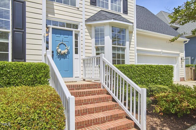 property entrance with an attached garage and a shingled roof