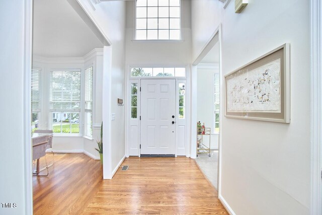 entrance foyer with a towering ceiling, baseboards, visible vents, and light wood-type flooring