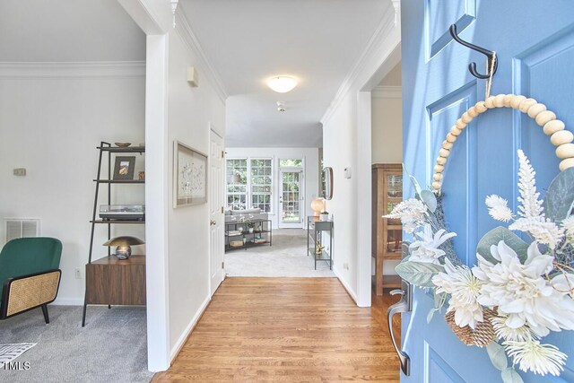 foyer featuring visible vents, ornamental molding, baseboards, light wood-style floors, and light colored carpet