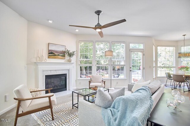living room with a high end fireplace, baseboards, a ceiling fan, and a healthy amount of sunlight