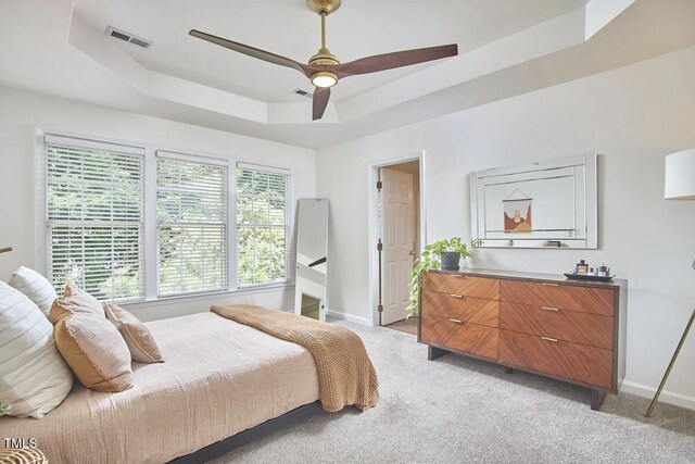 bedroom featuring light colored carpet, baseboards, a tray ceiling, and visible vents