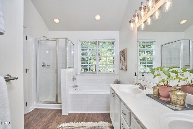 full bath with double vanity, a garden tub, a stall shower, wood finished floors, and a sink