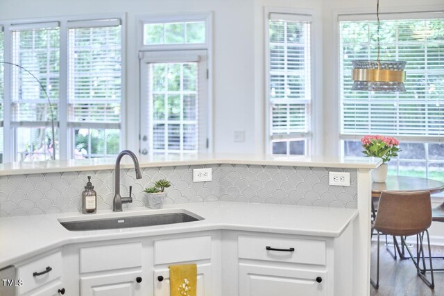 kitchen with backsplash, white cabinetry, a sink, and light countertops