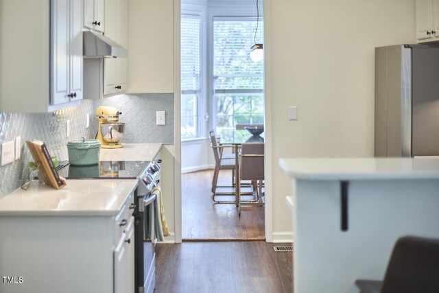 kitchen featuring decorative backsplash, dark wood-type flooring, light countertops, under cabinet range hood, and appliances with stainless steel finishes