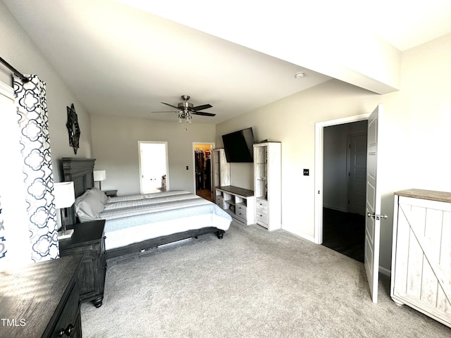 carpeted bedroom with a closet, a walk in closet, baseboards, and a ceiling fan