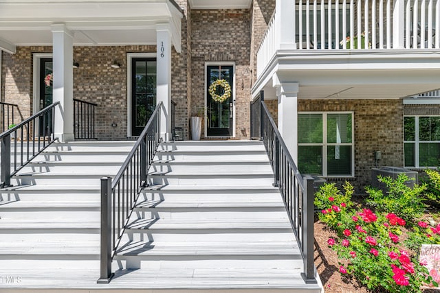 property entrance featuring central air condition unit, a balcony, a porch, and brick siding