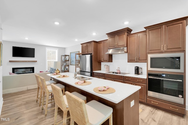 kitchen with light wood-style floors, a breakfast bar area, under cabinet range hood, a sink, and black appliances