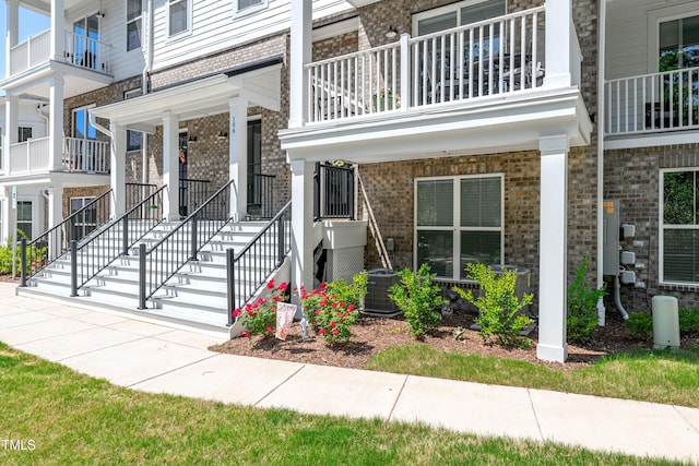 entrance to property with brick siding, central air condition unit, a balcony, and a porch