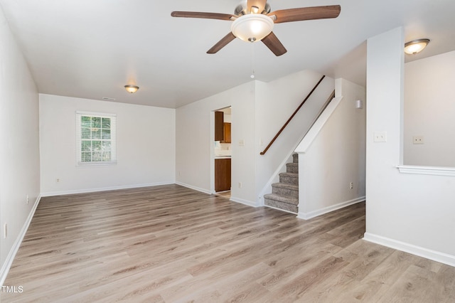 unfurnished living room featuring light wood-style flooring, ceiling fan, stairway, and baseboards