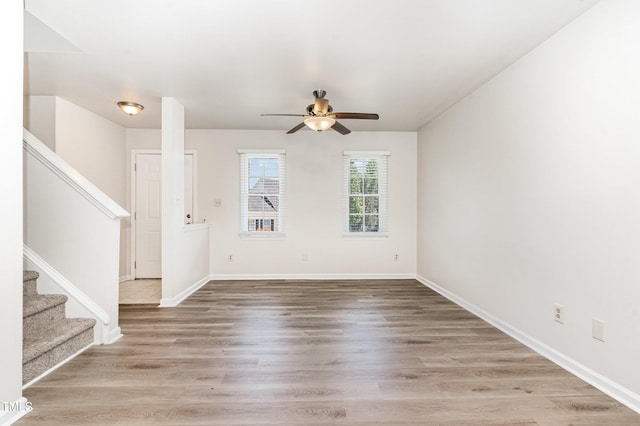 unfurnished living room with stairs, a ceiling fan, wood finished floors, and baseboards