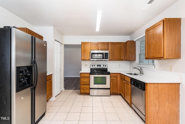 kitchen with appliances with stainless steel finishes, a sink, light countertops, and light tile patterned flooring