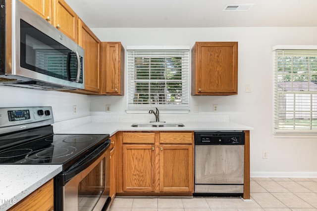 kitchen featuring appliances with stainless steel finishes, a sink, light countertops, light tile patterned flooring, and brown cabinets