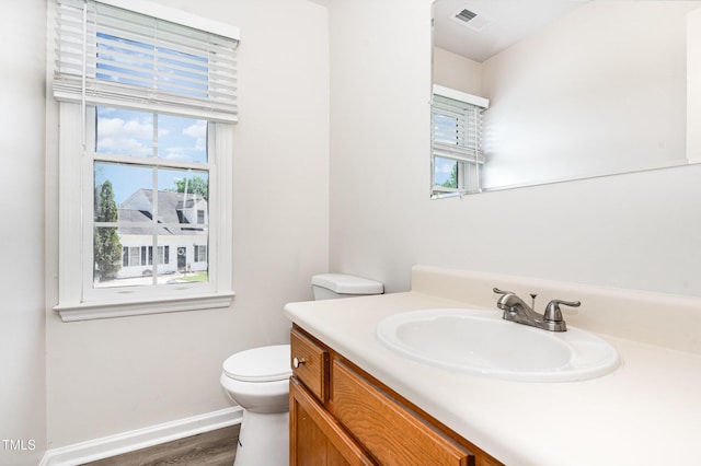 half bath featuring plenty of natural light, vanity, toilet, and wood finished floors
